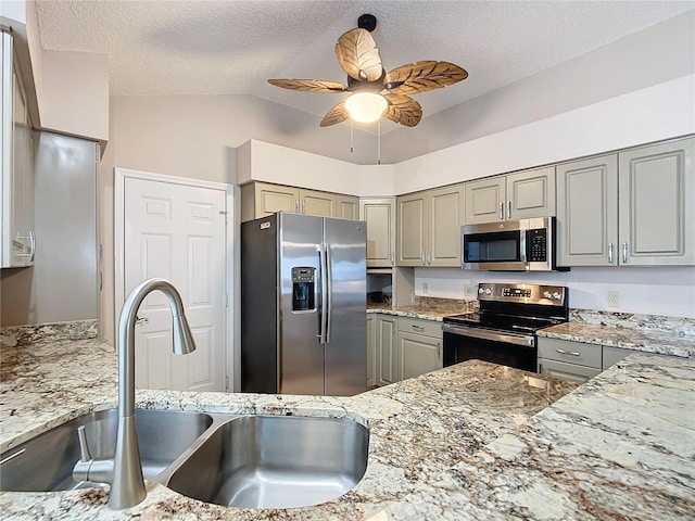 kitchen with ceiling fan, sink, stainless steel appliances, light stone counters, and a textured ceiling