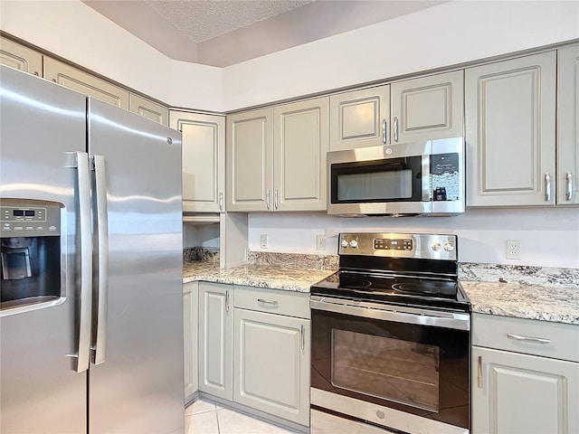 kitchen featuring light stone countertops, light tile patterned floors, a textured ceiling, and stainless steel appliances