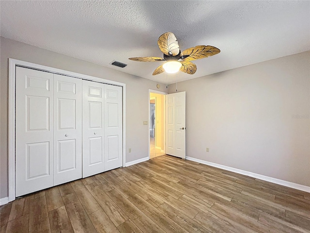 unfurnished bedroom with ceiling fan, a closet, hardwood / wood-style floors, and a textured ceiling