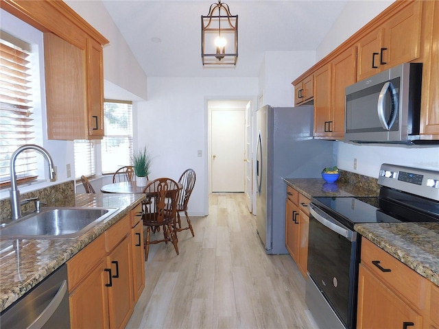 kitchen featuring sink, vaulted ceiling, dark stone countertops, appliances with stainless steel finishes, and light hardwood / wood-style floors