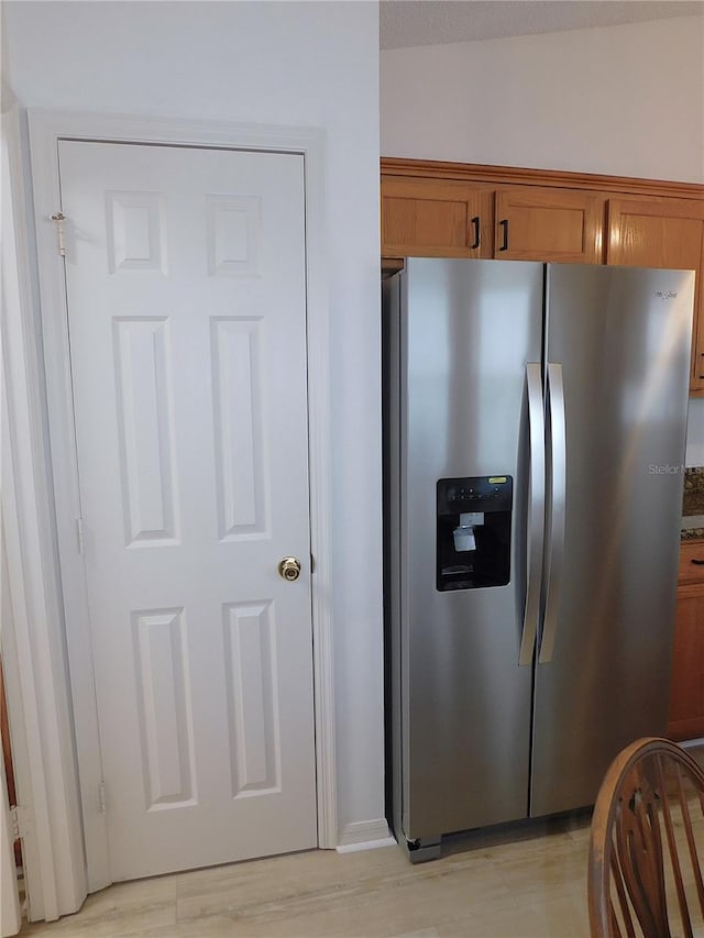 kitchen with dark stone counters, stainless steel refrigerator with ice dispenser, and light wood-type flooring