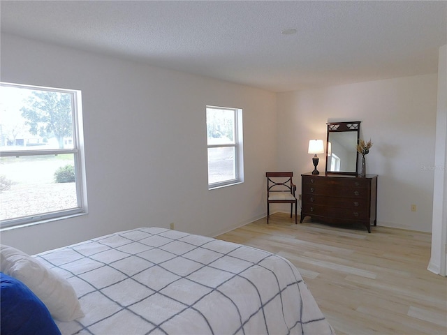 bedroom with multiple windows, light hardwood / wood-style flooring, and a textured ceiling