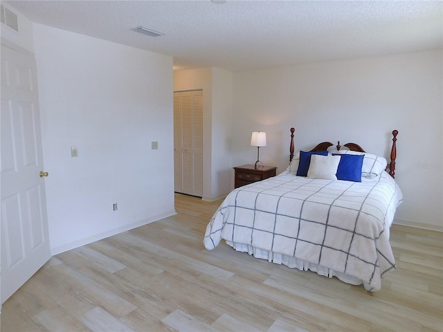 bedroom with a textured ceiling, light wood-type flooring, and a closet