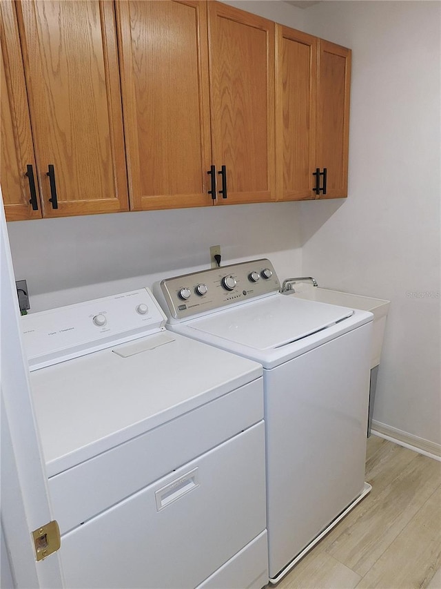 laundry area featuring washer and clothes dryer, cabinets, and light wood-type flooring