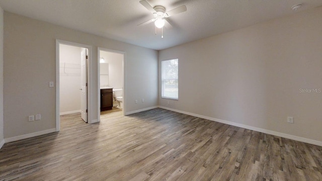 unfurnished bedroom with ensuite bathroom, a walk in closet, ceiling fan, light wood-type flooring, and a closet