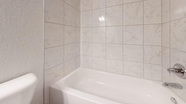 bathroom featuring toilet and tiled shower / bath