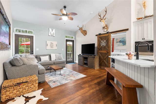 living room with sink, ceiling fan, high vaulted ceiling, dark hardwood / wood-style floors, and a barn door