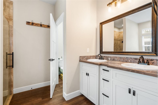 bathroom with wood-type flooring, a shower with shower door, vanity, and toilet