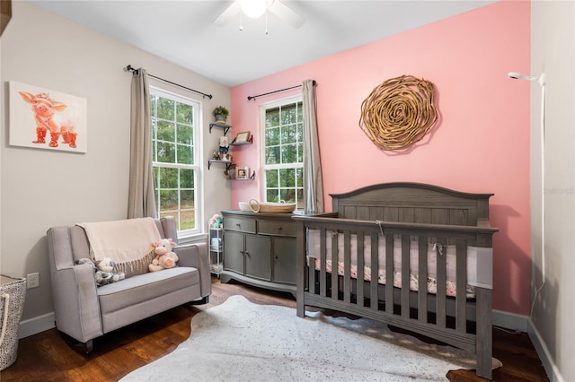 bedroom with a crib, dark hardwood / wood-style floors, and ceiling fan