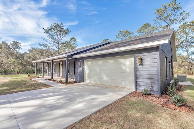 ranch-style home with central AC unit, covered porch, and a garage