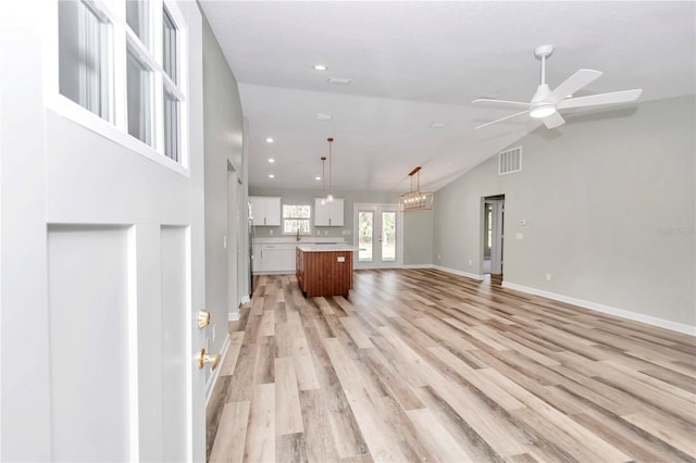 unfurnished living room with ceiling fan with notable chandelier, lofted ceiling, french doors, and light wood-type flooring