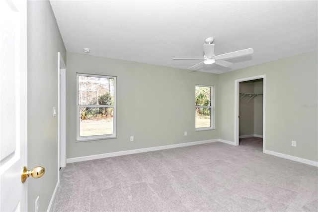 unfurnished bedroom with ceiling fan, light colored carpet, a walk in closet, and multiple windows