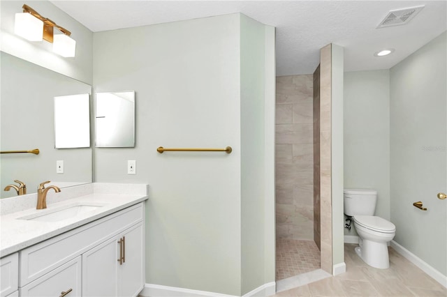 bathroom with toilet, vanity, a tile shower, and tile patterned flooring