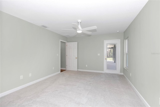 empty room with carpet flooring, a ceiling fan, visible vents, and baseboards