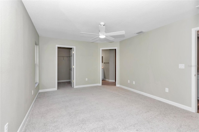 unfurnished bedroom with a spacious closet, visible vents, baseboards, light colored carpet, and a ceiling fan