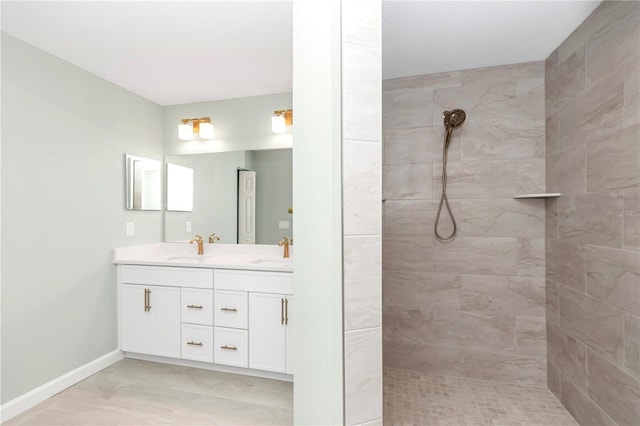 full bathroom featuring a sink, baseboards, double vanity, and a tile shower