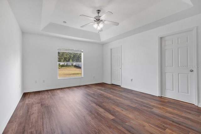 unfurnished bedroom featuring a tray ceiling, ceiling fan, and dark wood-type flooring