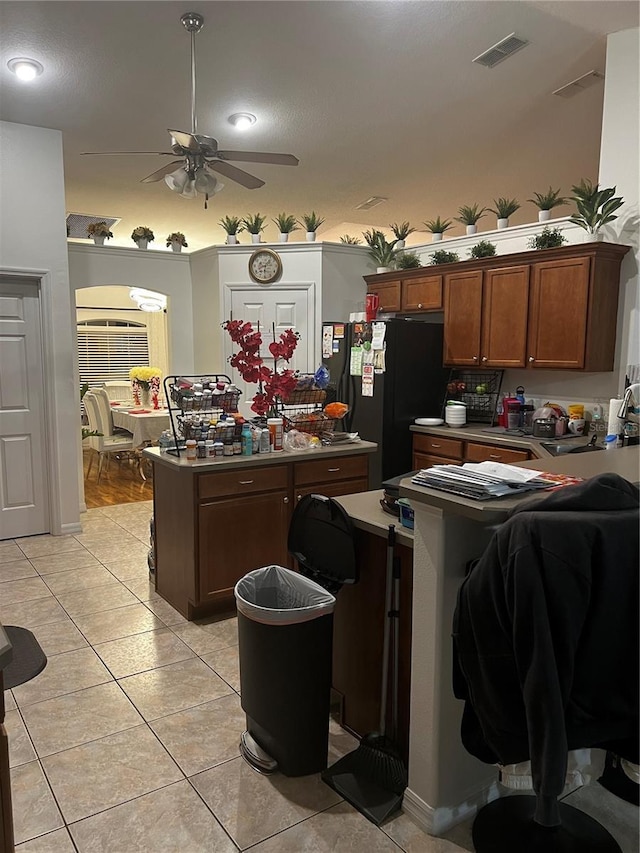 kitchen with ceiling fan, sink, a kitchen island, black fridge, and light tile patterned floors