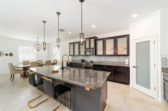 kitchen featuring a breakfast bar, stainless steel appliances, a kitchen island with sink, sink, and decorative light fixtures