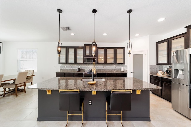 kitchen with decorative backsplash, appliances with stainless steel finishes, pendant lighting, and an island with sink