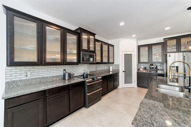 kitchen with backsplash, dark stone countertops, sink, and stainless steel appliances