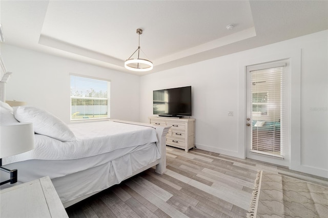 bedroom with access to exterior, a raised ceiling, and light wood-type flooring