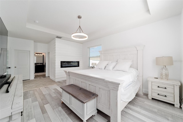 bedroom featuring a raised ceiling, a large fireplace, and light hardwood / wood-style floors