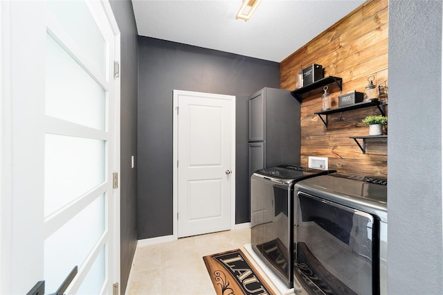 washroom with wood walls, light tile patterned flooring, and washer and dryer