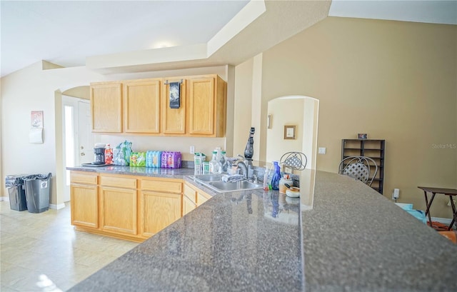 kitchen with light brown cabinetry, sink, and lofted ceiling