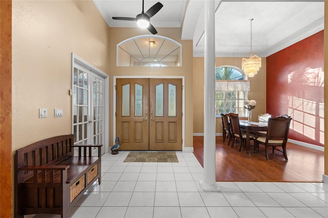 tiled entrance foyer with ceiling fan with notable chandelier, decorative columns, crown molding, and french doors