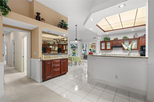 kitchen with ceiling fan, tasteful backsplash, light tile patterned flooring, light stone counters, and kitchen peninsula