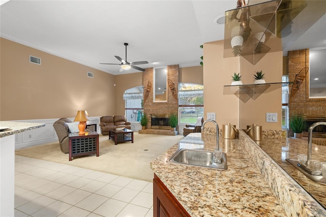 kitchen with ceiling fan, sink, crown molding, a fireplace, and light tile patterned flooring