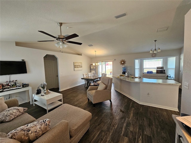 living area featuring visible vents, dark wood-type flooring, ceiling fan with notable chandelier, arched walkways, and lofted ceiling