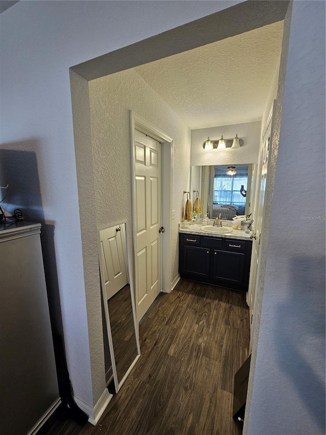 bathroom with a textured ceiling, wood finished floors, baseboards, vanity, and a textured wall