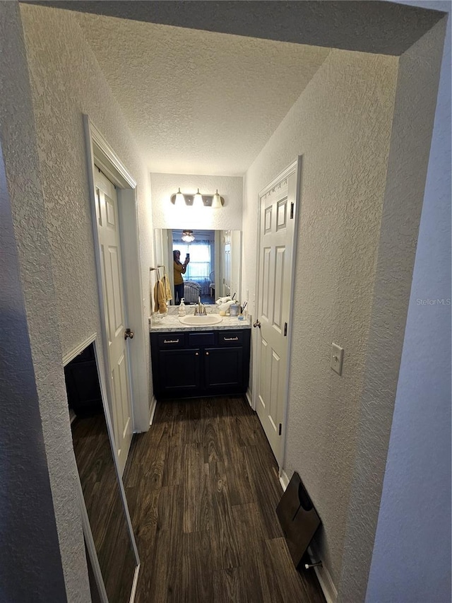 hallway with dark wood finished floors, a textured ceiling, a textured wall, and a sink