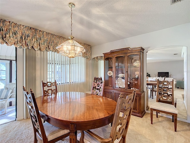 dining area with a notable chandelier, light colored carpet, a textured ceiling, and a wealth of natural light