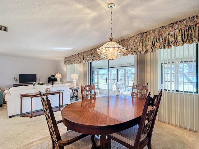 dining space with light colored carpet, a textured ceiling, and a chandelier