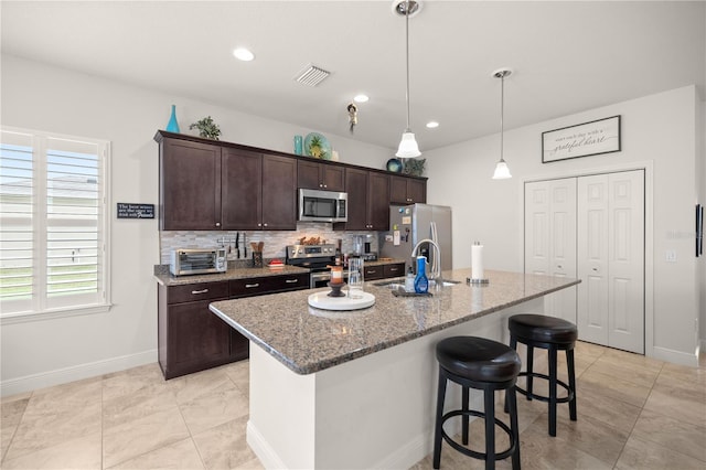 kitchen featuring dark brown cabinetry, stainless steel appliances, sink, a center island with sink, and stone countertops