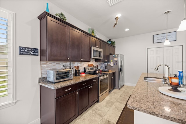 kitchen featuring light stone countertops, sink, backsplash, pendant lighting, and appliances with stainless steel finishes