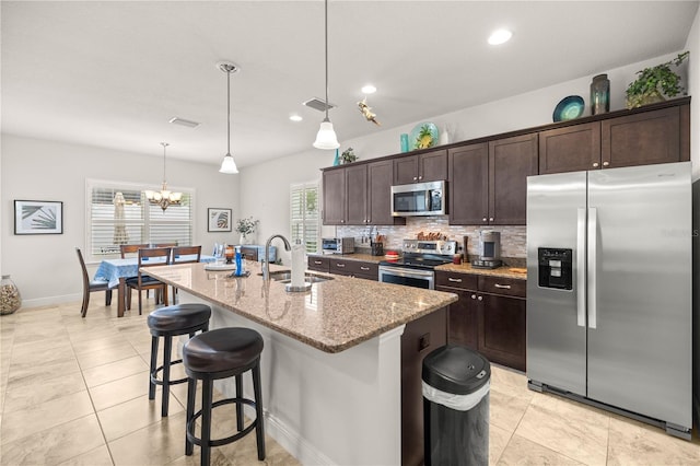 kitchen featuring light stone countertops, sink, pendant lighting, a kitchen island with sink, and appliances with stainless steel finishes