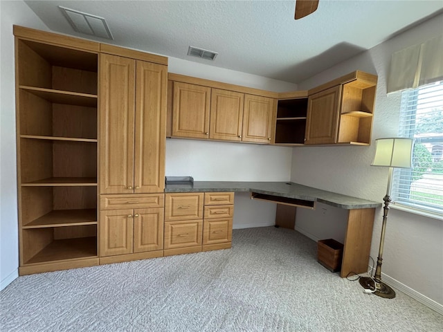 unfurnished office with light carpet, ceiling fan, built in desk, and a textured ceiling