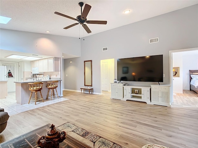 unfurnished living room with a skylight, high vaulted ceiling, ceiling fan, and light hardwood / wood-style flooring