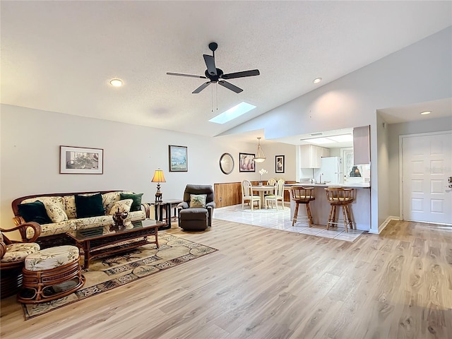 living room featuring a textured ceiling, light hardwood / wood-style flooring, ceiling fan, and vaulted ceiling with skylight