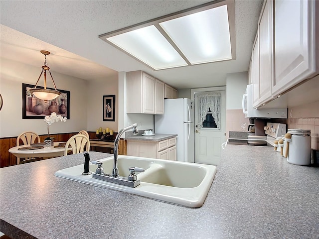 kitchen with stove, sink, hanging light fixtures, white fridge, and white cabinetry