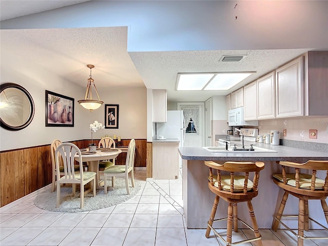 kitchen featuring kitchen peninsula, sink, light tile patterned floors, decorative light fixtures, and wood walls