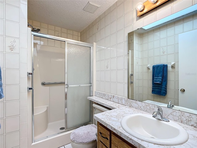 bathroom with vanity, a shower with door, toilet, a textured ceiling, and tile walls