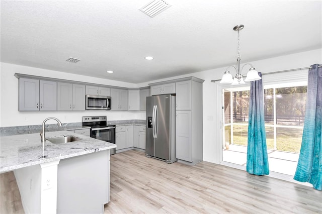 kitchen featuring kitchen peninsula, appliances with stainless steel finishes, gray cabinetry, sink, and hanging light fixtures