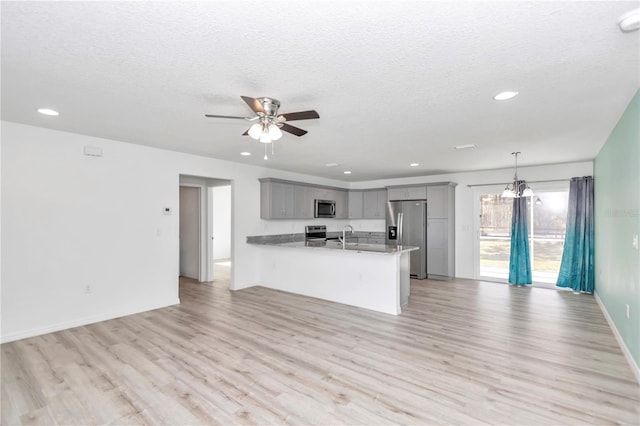 kitchen with hanging light fixtures, gray cabinets, a textured ceiling, kitchen peninsula, and stainless steel appliances