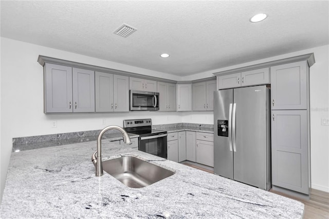 kitchen featuring sink, gray cabinets, light stone countertops, a textured ceiling, and stainless steel appliances