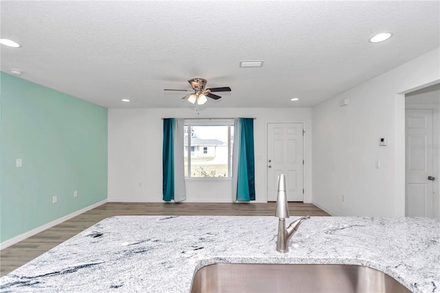 interior space with light stone counters, a textured ceiling, ceiling fan, sink, and hardwood / wood-style flooring